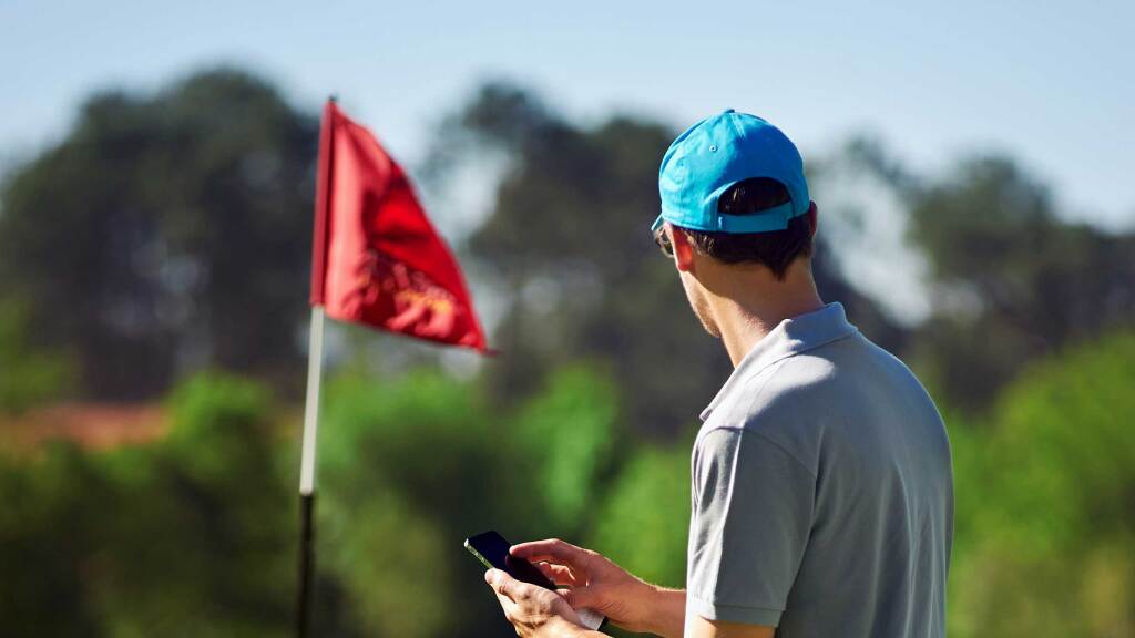 Golfer on course using mobile phone while looking at red flag over hole